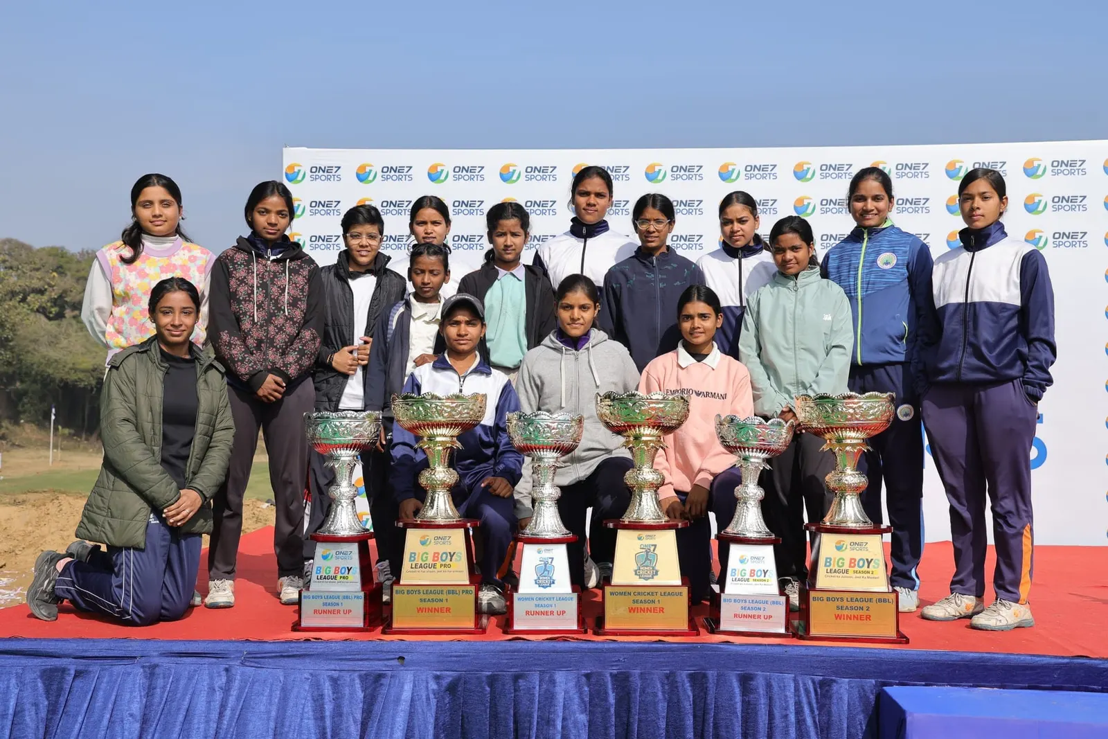 Young women on a stage with One7 Sports league trophies